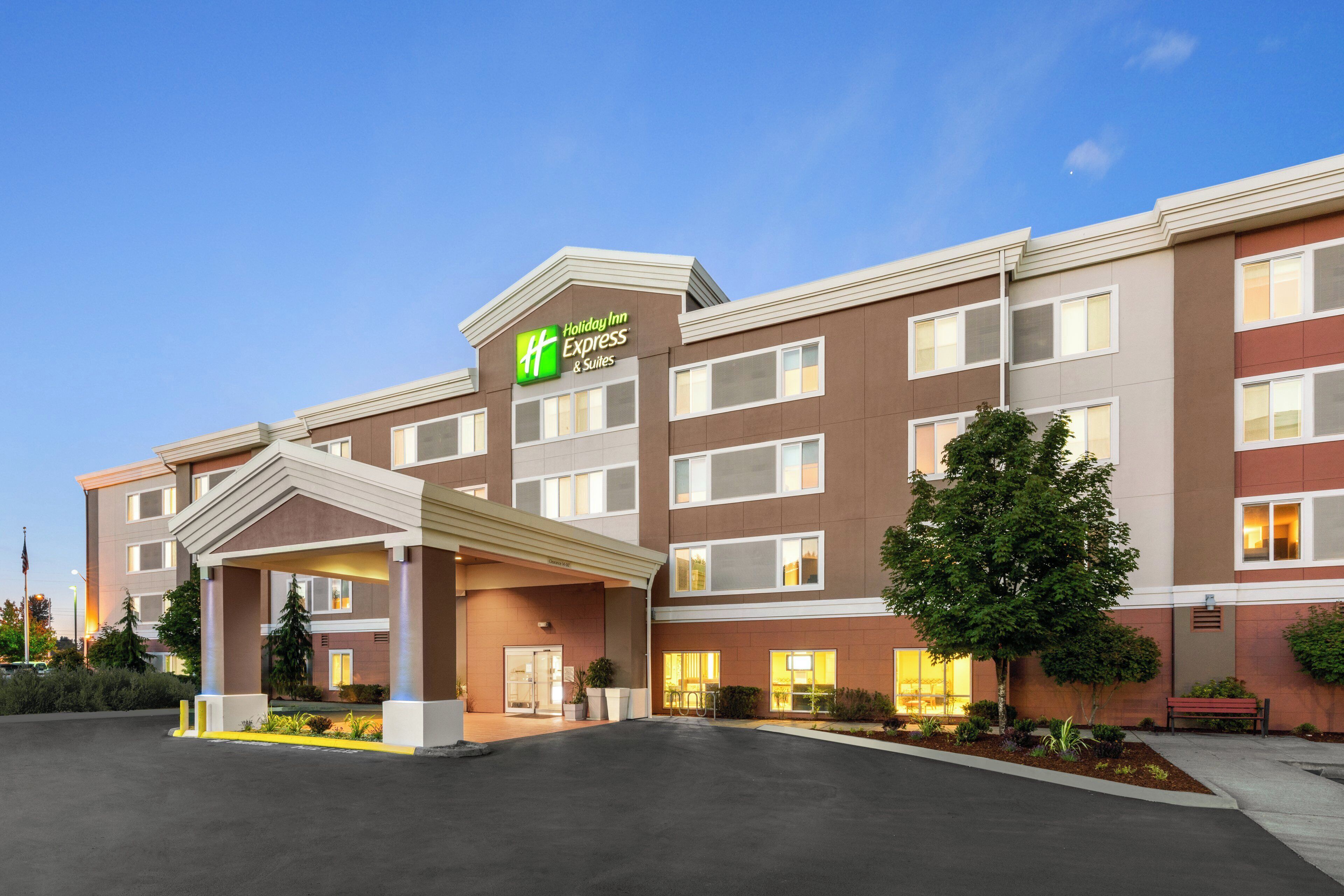 A Holiday Inn Express & Suites building with a covered entrance, multiple windows, and a well-lit facade.