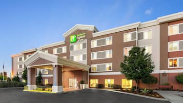 A Holiday Inn Express & Suites building with a covered entrance, multiple windows, and a well-lit facade.