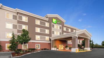 A Holiday Inn Express & Suites building with a covered entrance, multiple windows, and a parking lot.