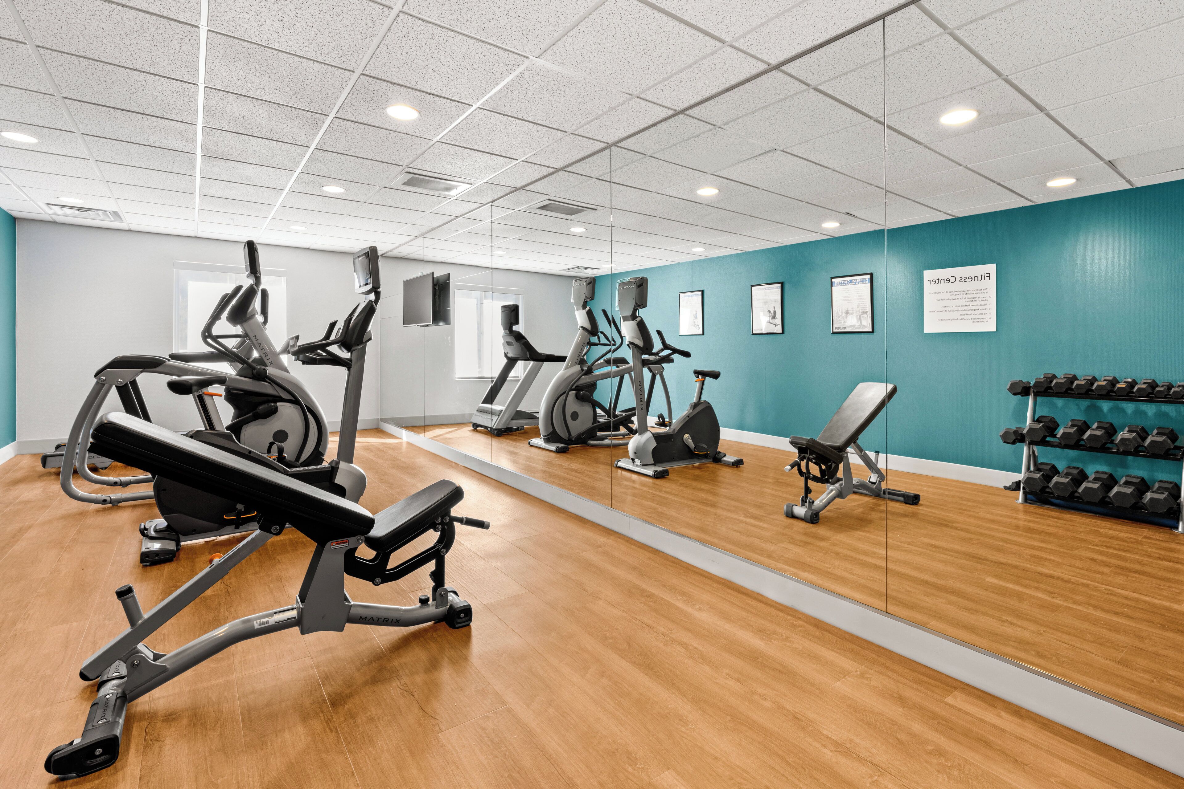 Une salle de sport équipée de matériel d’exercice, d’un miroir et d’un mur où sont affichées des posters d’information.
