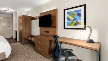 Una camera d'albergo con una scrivania in legno, una TV a schermo piatto, una sedia moderna e un quadro astratto appeso alla parete.