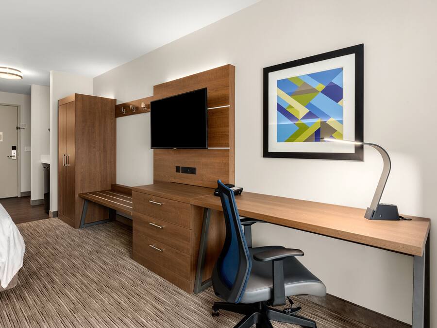 Una camera d'albergo con una scrivania in legno, una TV a schermo piatto, una sedia moderna e un quadro astratto appeso alla parete.