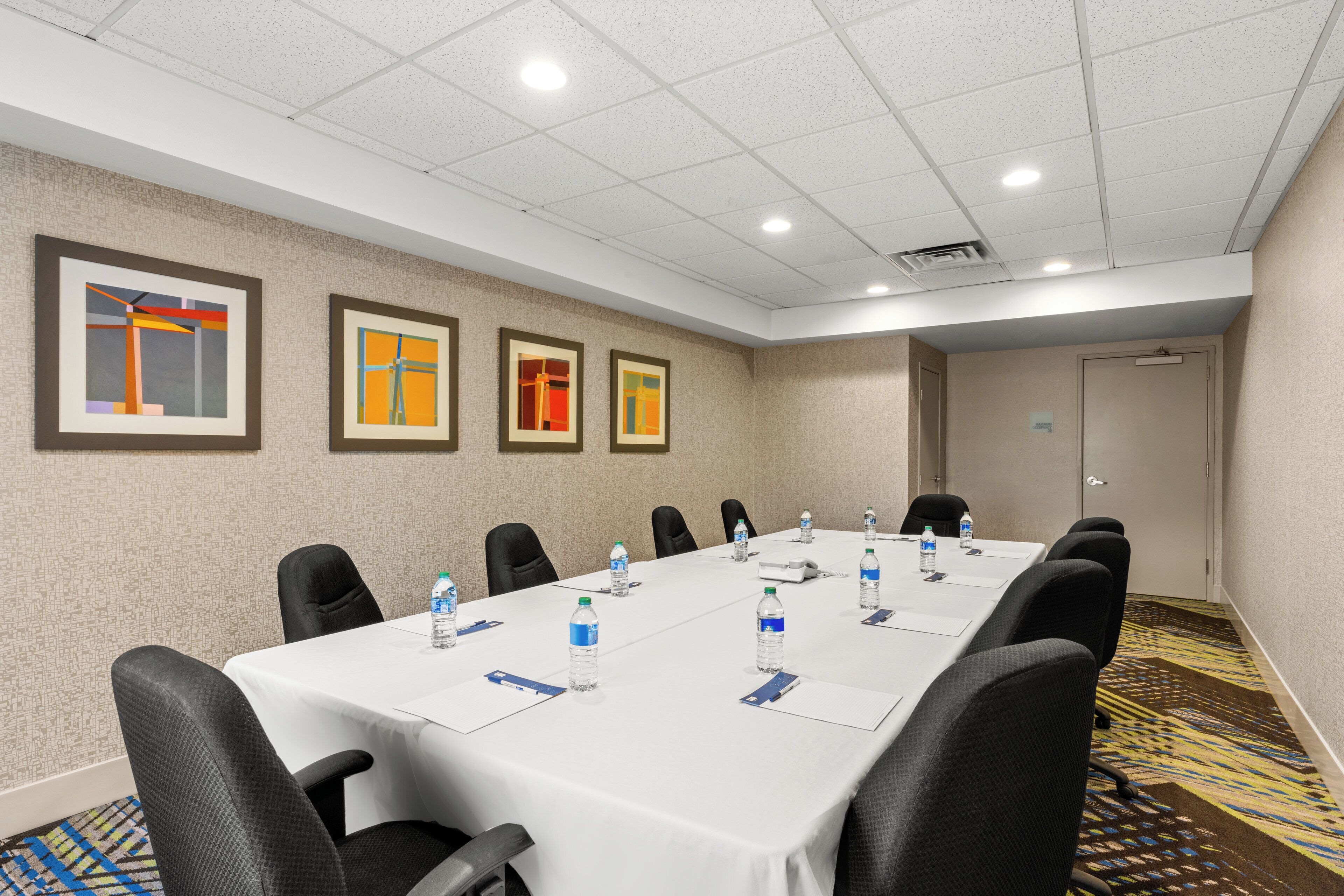 Un salón de conferencias con una larga mesa, sillas, botellas de agua y cuadros en la pared.