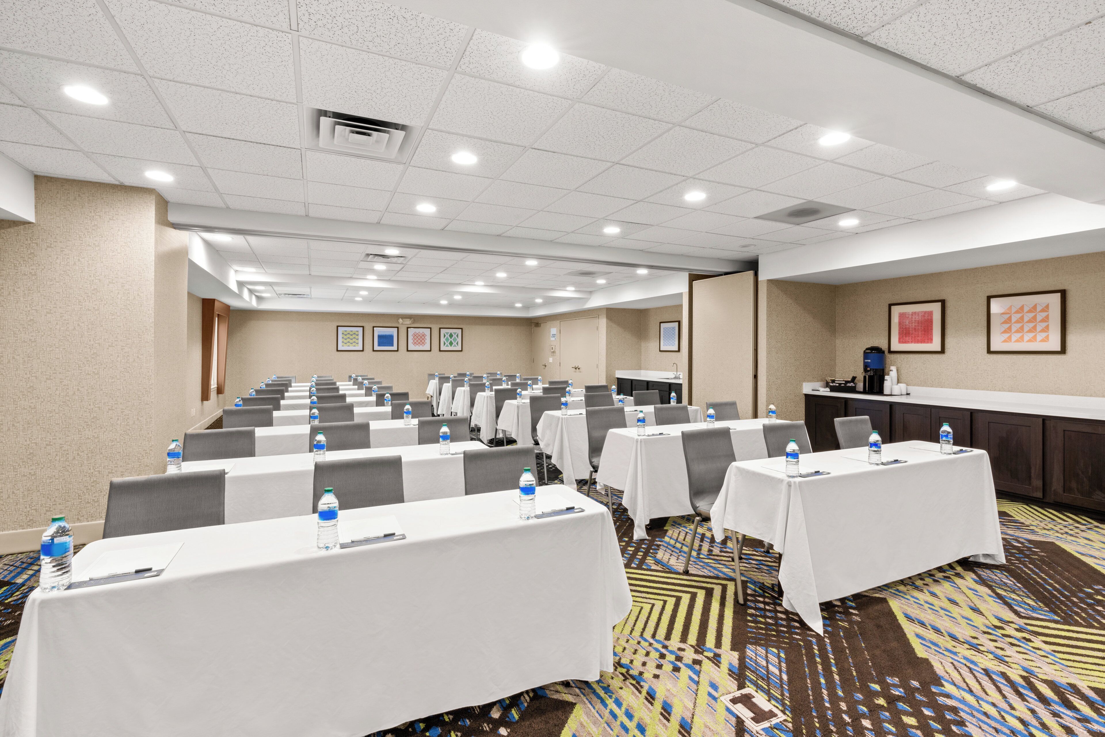 A conference room with rows of tables, chairs, and water bottles, equipped with a projector and a whiteboard.