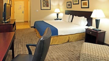 Una habitación de hotel con cama, lámparas de noche, escritorio con televisor, una silla y un reposapiés.