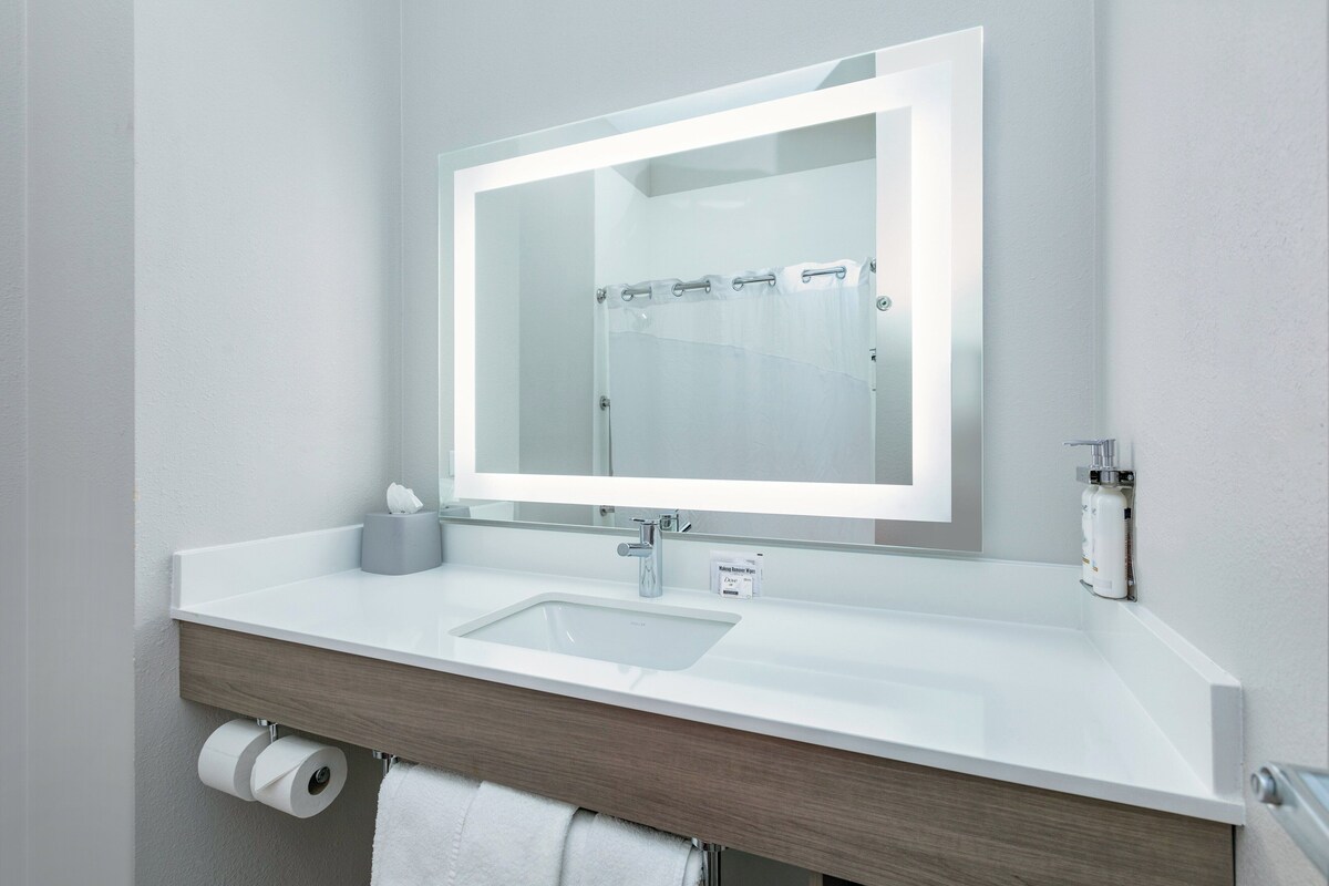 A modern bathroom with a white sink, a mirror, and a shower curtain.
