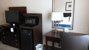 A hotel room with a television, microwave, and a small desk with a lamp.