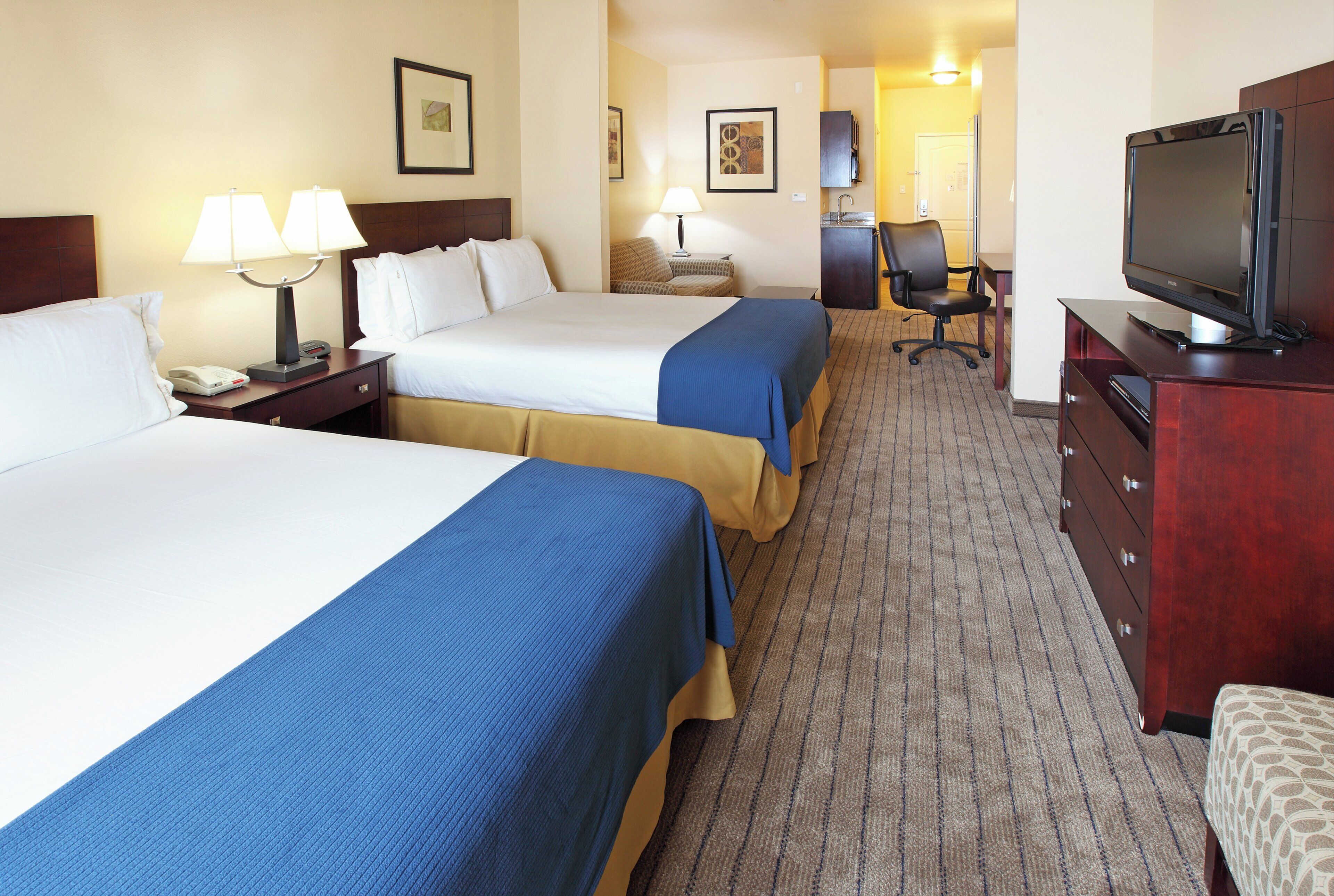A hotel room with two beds, a desk with a chair, a television, and a bathroom visible in the background.