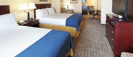A hotel room with two beds, a desk with a chair, a television, and a bathroom visible in the background.