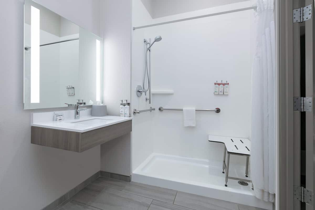 A modern bathroom with a large mirror, two sinks, a bathtub, and a shower.