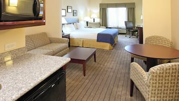 Habitación de hotel con kitchenette, cama, sofá, mesa de comedor y una silla.