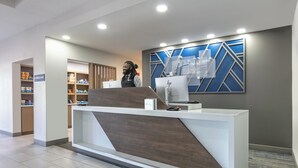 Un comptoir d’accueil au design moderne, une machine à café et un panneau indiquant l’emplacement d’une imprimerie.