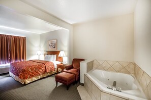 A hotel room with a large bed, a sitting area with a chair and a table, a bathtub, and a window with curtains.