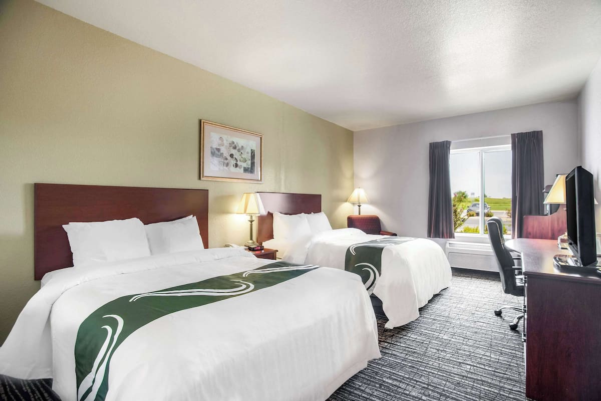 Une chambre d’hôtel avec deux lits, un bureau, une chaise et un téléviseur.