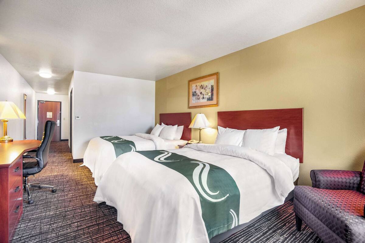 Une chambre d’hôtel avec un grand lit, un bureau avec une chaise, une lampe et un tableau encadré au mur.