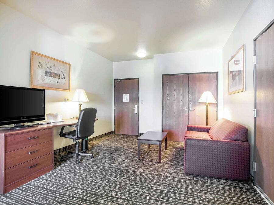 Una habitación de hotel con una televisión de pantalla plana, un escritorio con lámpara, una silla, una mesita, un sofá y dos puertas.