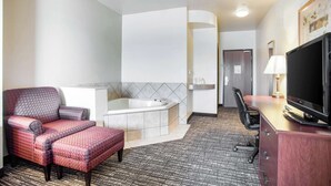 Une chambre d’hôtel avec un fauteuil rouge à revêtement en tissu, un canapé blanc, un grand téléviseur à écran plat, un bureau avec une lampe et une baignoire.