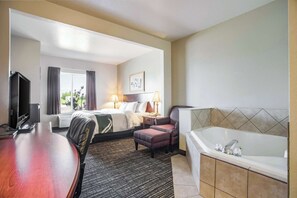 Habitación de hotel con cama, escritorio, silla, televisor, lámpara, un cuadro y una bañera.
