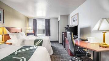 A hotel room with two beds, a desk with a lamp, a TV, and a window with curtains.