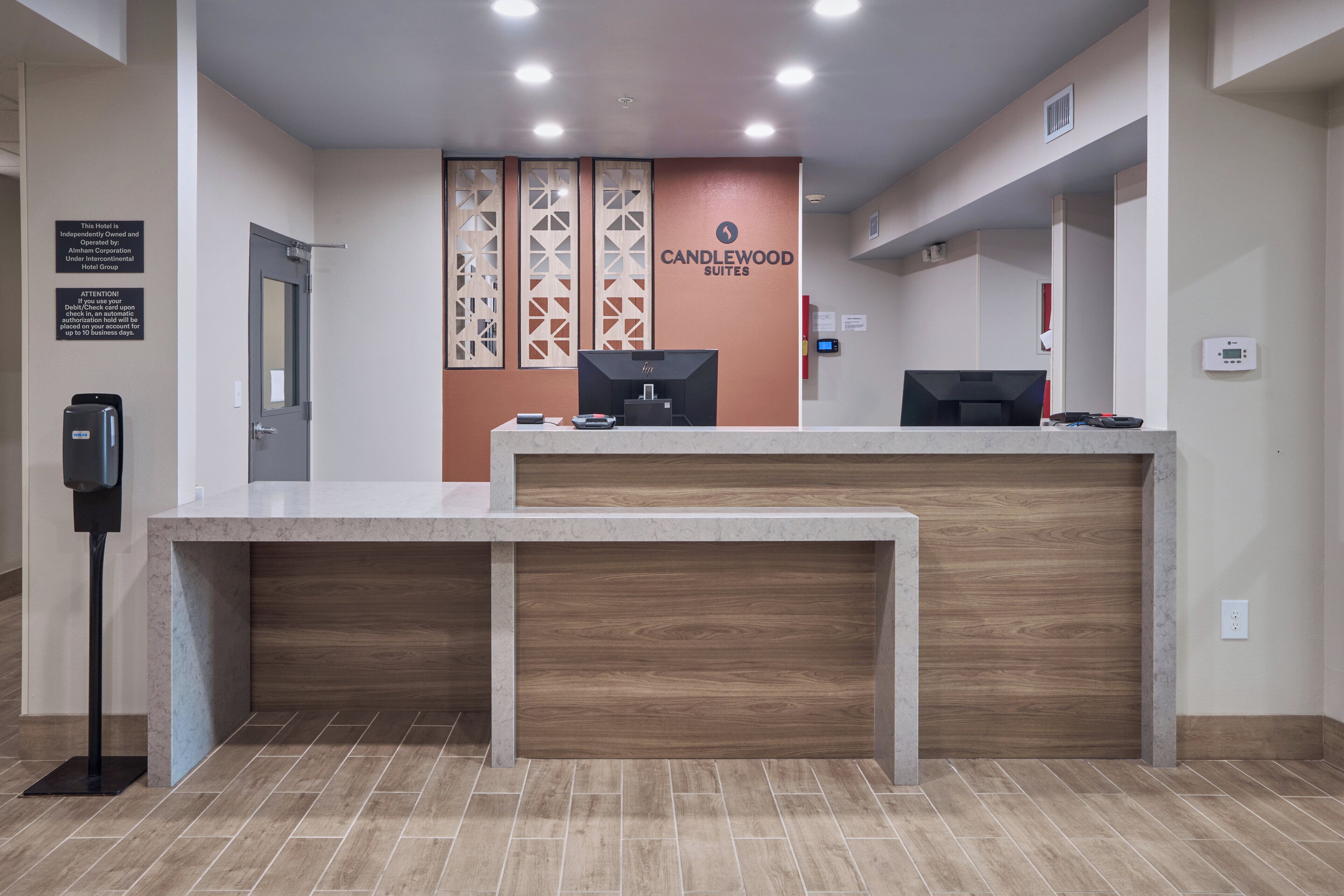 A reception desk with a modern design, a sign for Candlewood Suites, and a digital display.