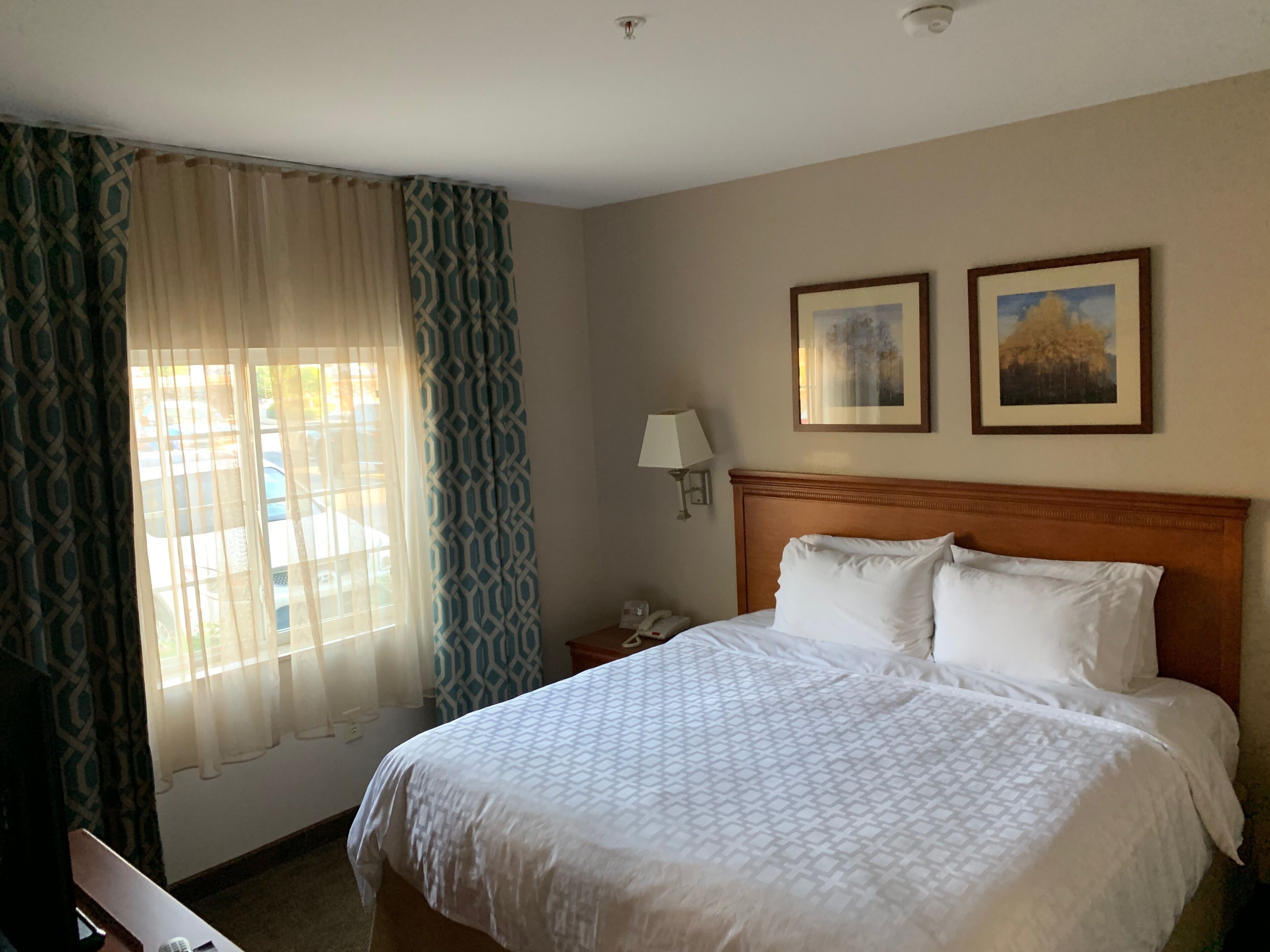 Una habitación de hotel con una cama, una mesita de noche, una lámpara y dos cuadros en la pared.