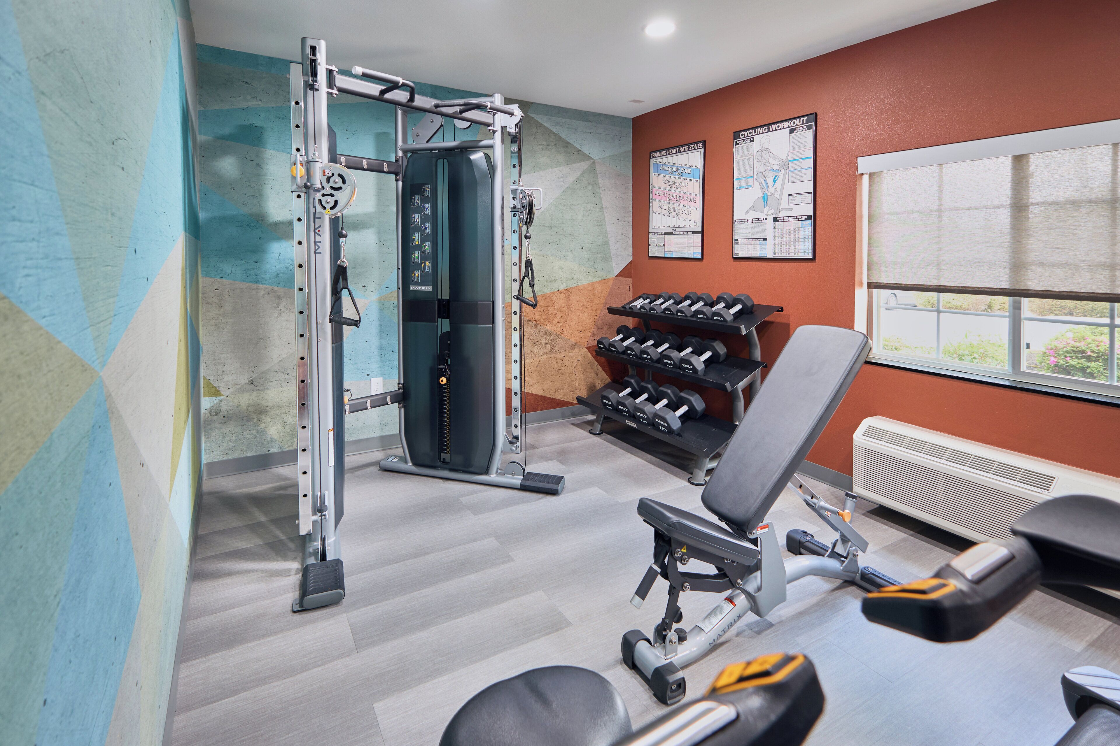 Un gimnasio con una máquina de pesas, mancuernas y un banco.