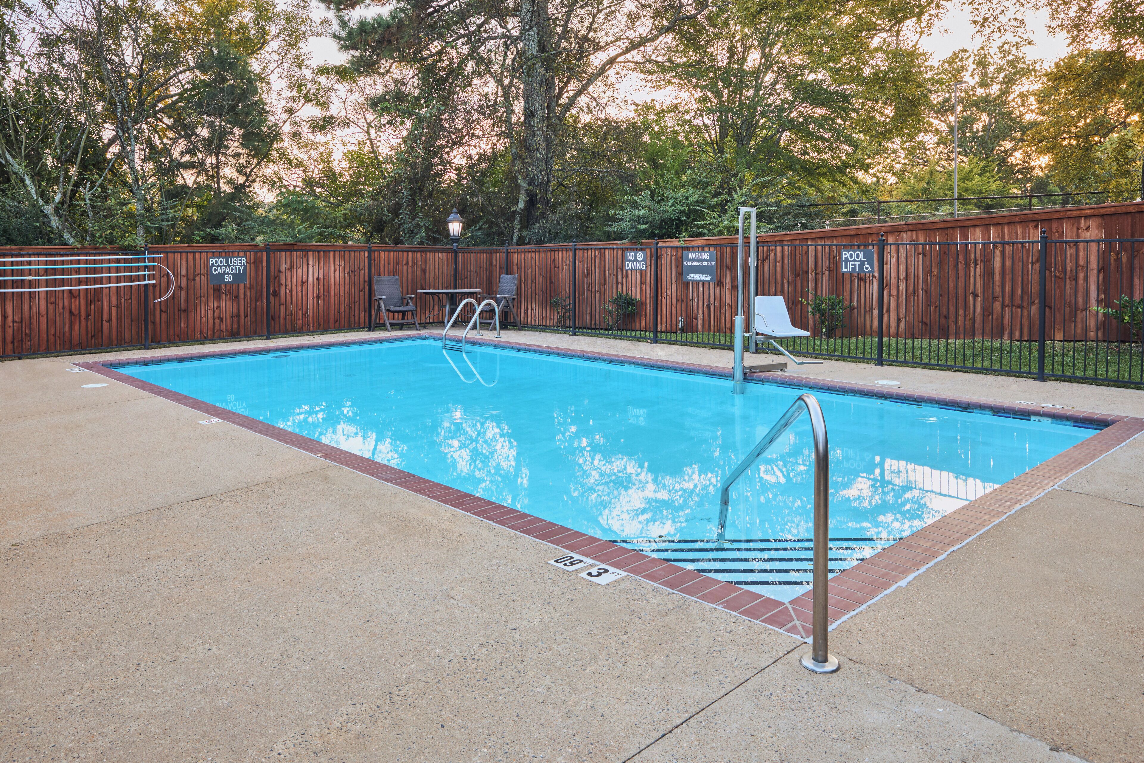 Una piscina rectangular con cerramiento de madera, una escalera metálica y algunas sillas de descanso.