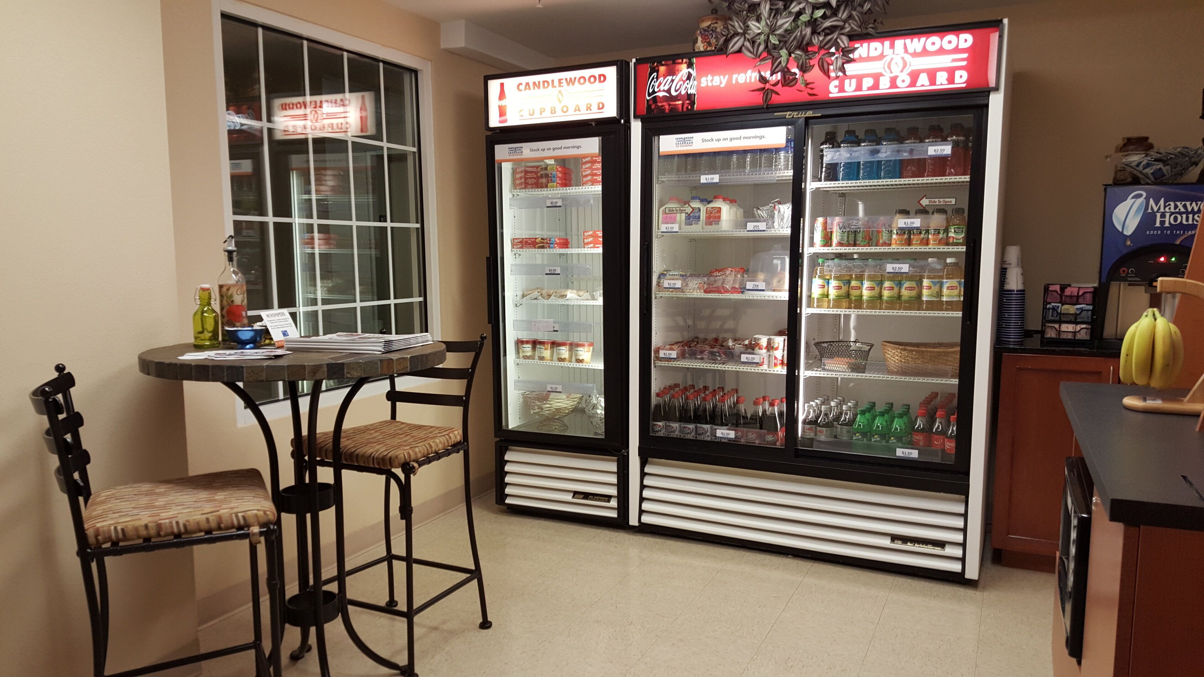 Una kitchenette con una mesa, sillas, un refrigerador lleno de bebidas y un microondas.