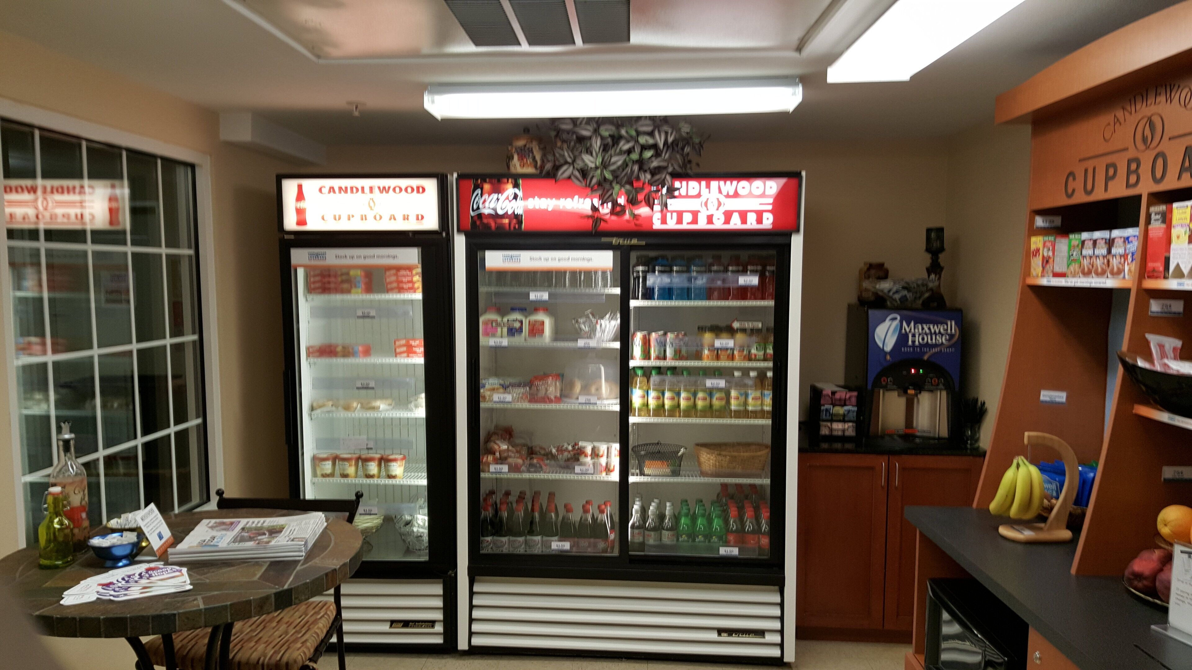 A kitchenette area with a refrigerator stocked with beverages, a coffee machine, and a display of canned goods.