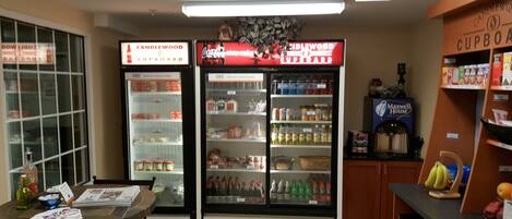 A kitchenette area with a refrigerator stocked with beverages, a coffee machine, and a display of canned goods.