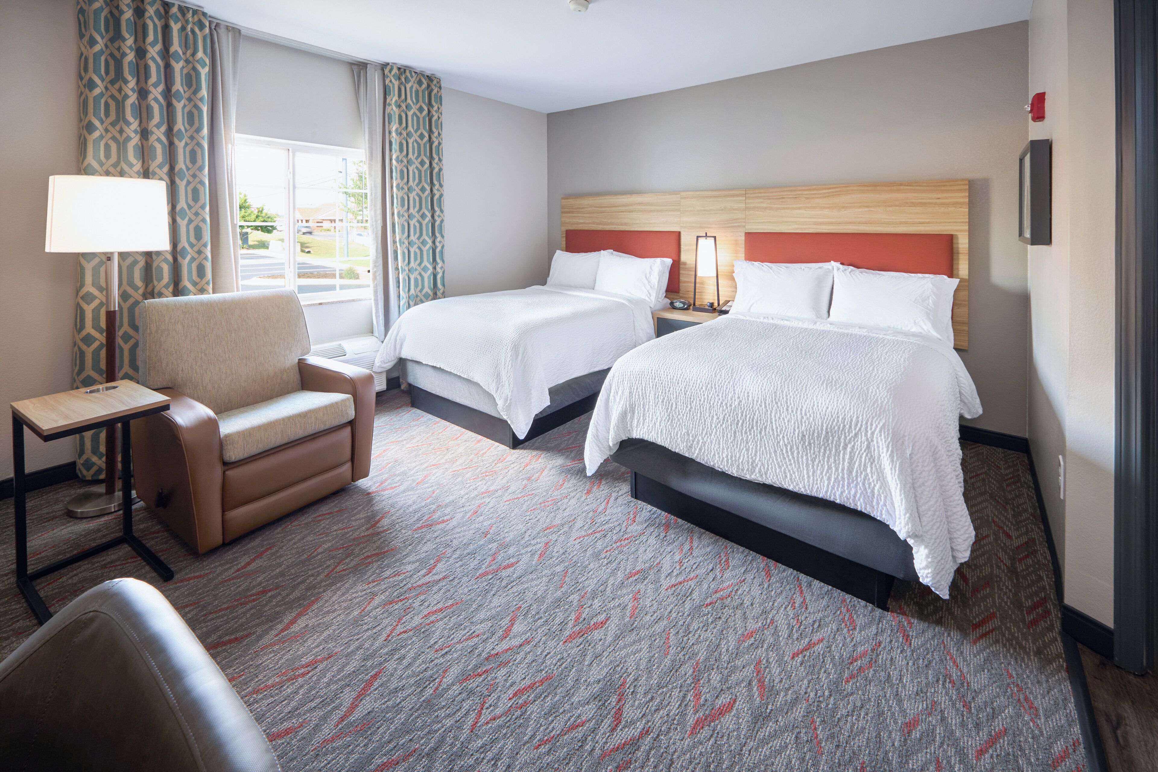 Ein Hotelzimmer mit zwei Betten, einem Schlafsofa, einem kleinen Tisch und einer Lampe.