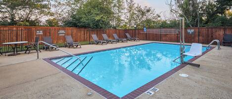A swimming pool with lounge chairs and a wooden fence.