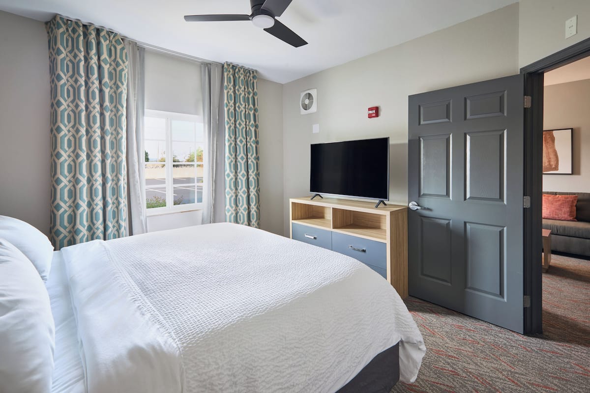 Ein Hotelzimmer mit Bett, Fernseher, Tür und einem Fenster mit Vorhängen.