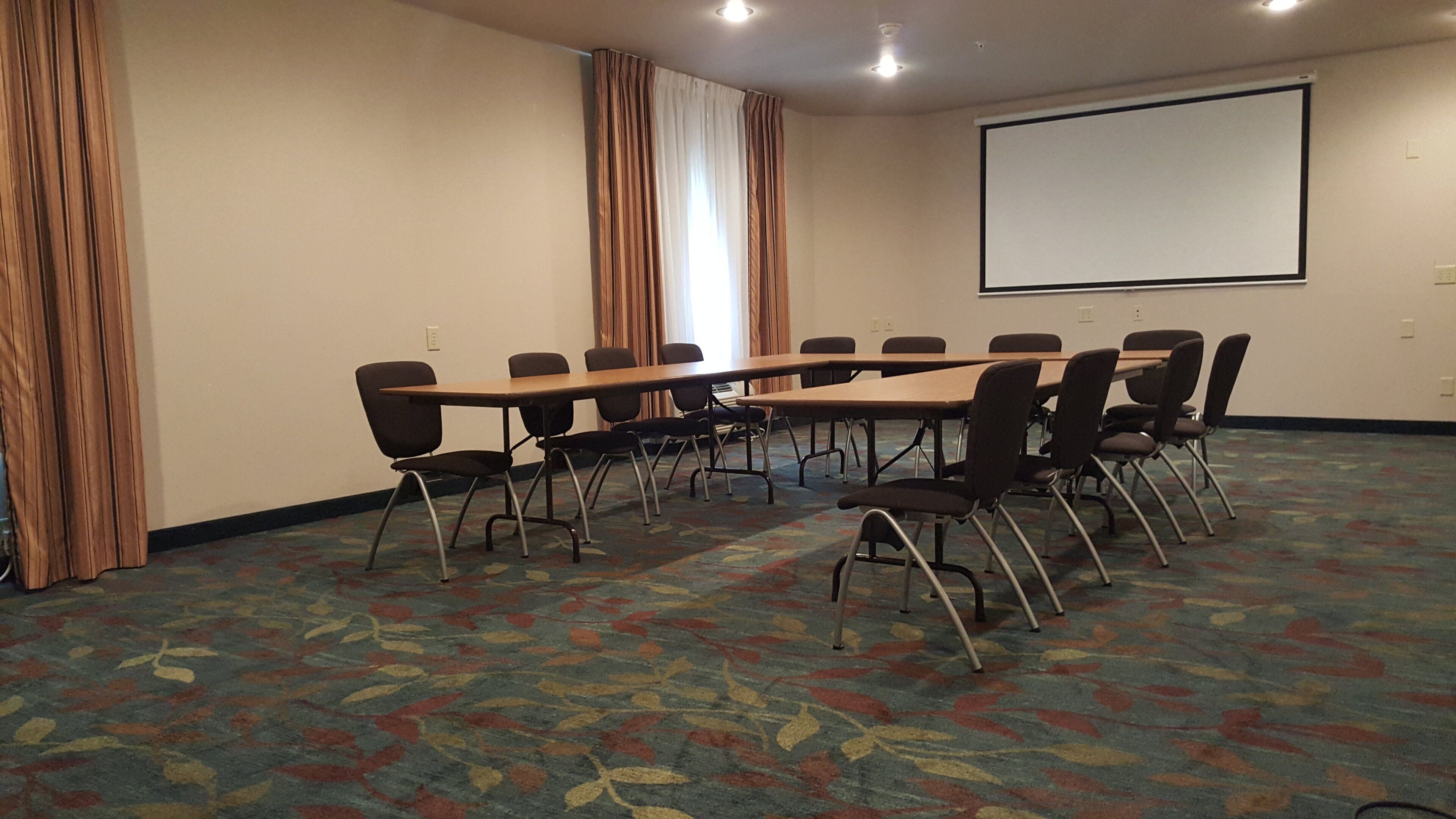 Ett konferensrum med ett långt bord, stolar, en projektorduk och gardiner.