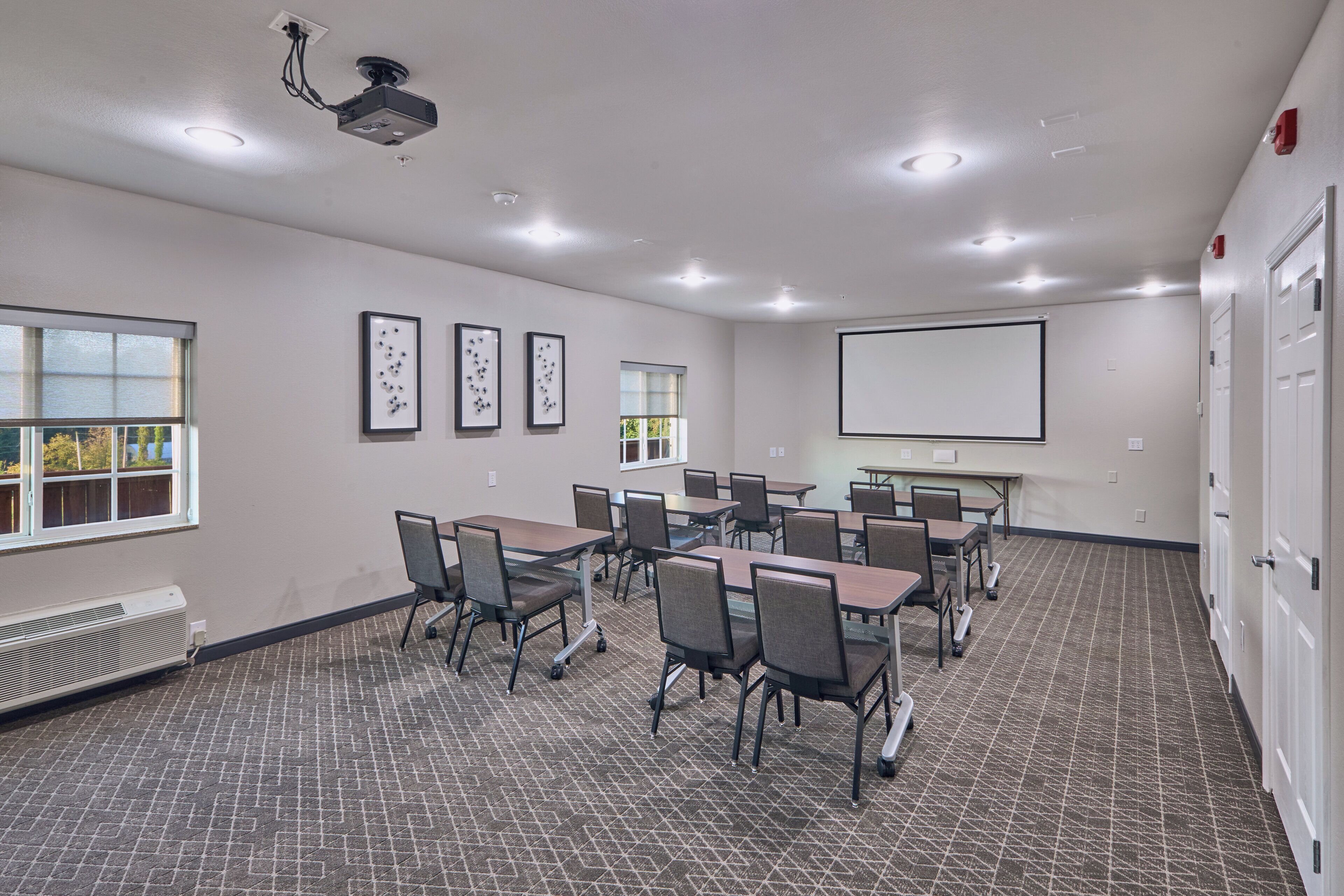 A conference room with tables and chairs, a projector, and a screen.