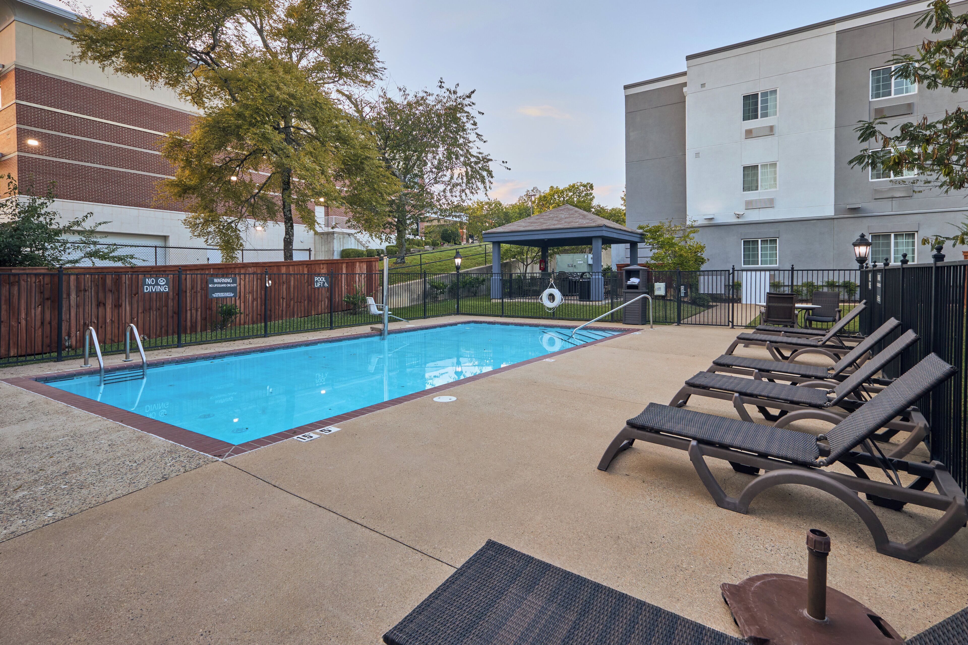 A swimming pool with lounge chairs and a gazebo in a courtyard.