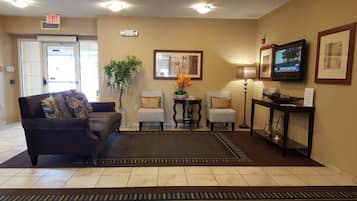 A hotel lobby with a sofa, two patterned chairs, a small table with a plant, a lamp, and a television on a stand.