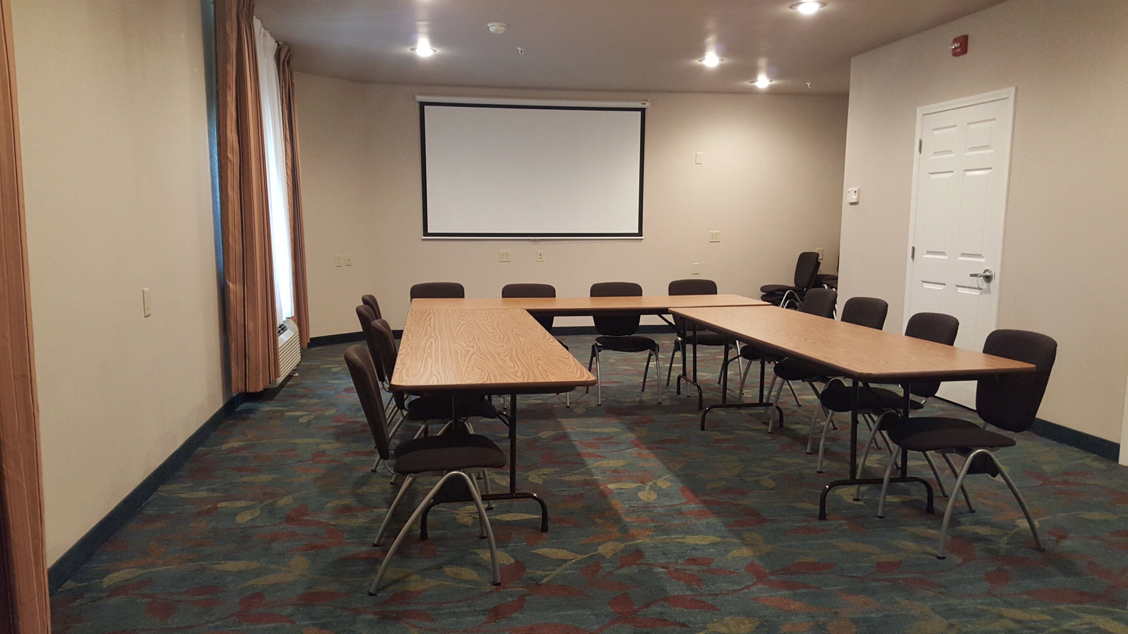 A conference room with a large screen, multiple tables, and chairs.