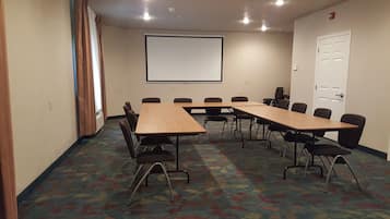 A conference room with a large screen, multiple tables, and chairs.