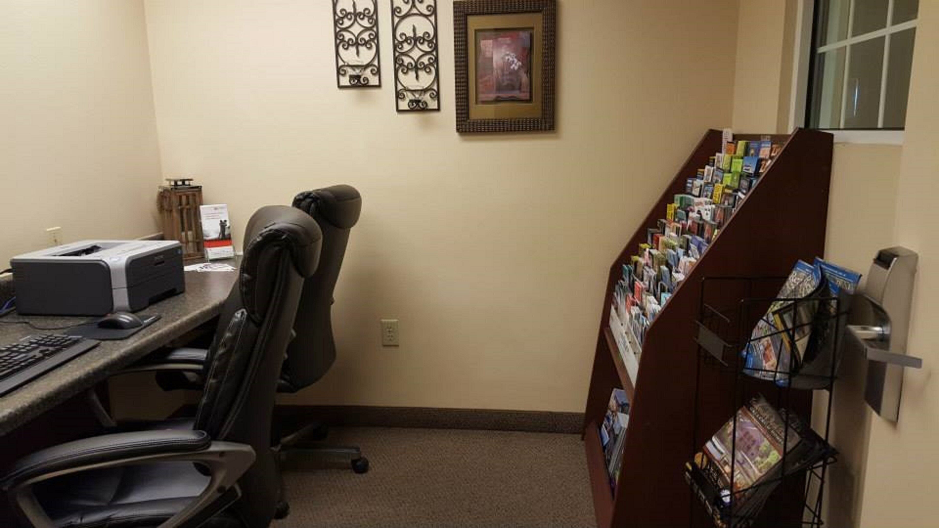 A small office space with a desk, printer, chair, and a magazine rack.