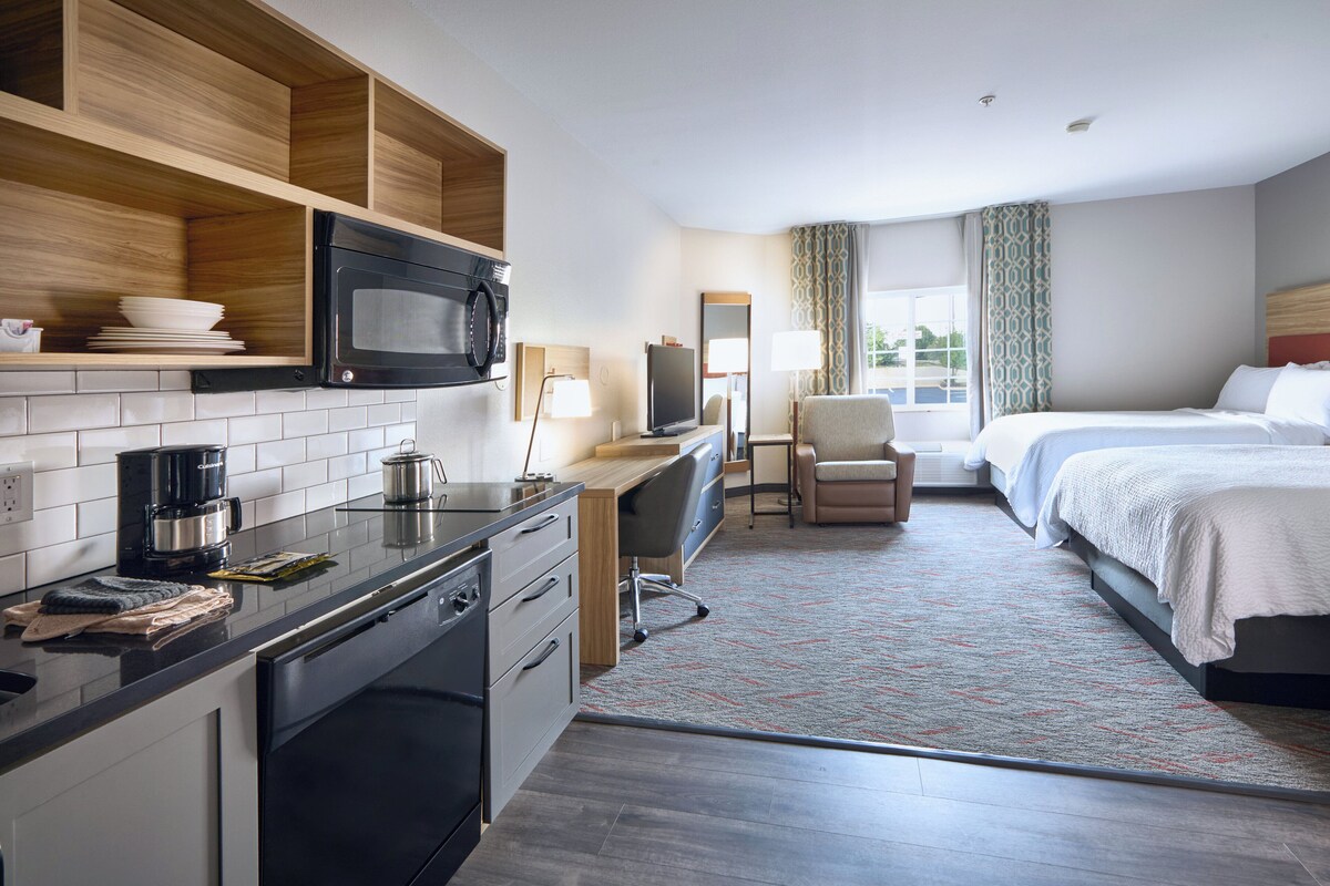 Ein Hotelzimmer mit einer Küchenzeile, einem Bett, einem Schreibtisch und einem Stuhl.