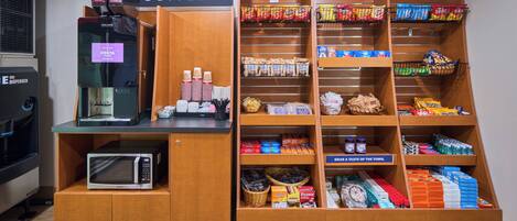 A coffee station with a coffee machine, a microwave, and various snacks and beverages.