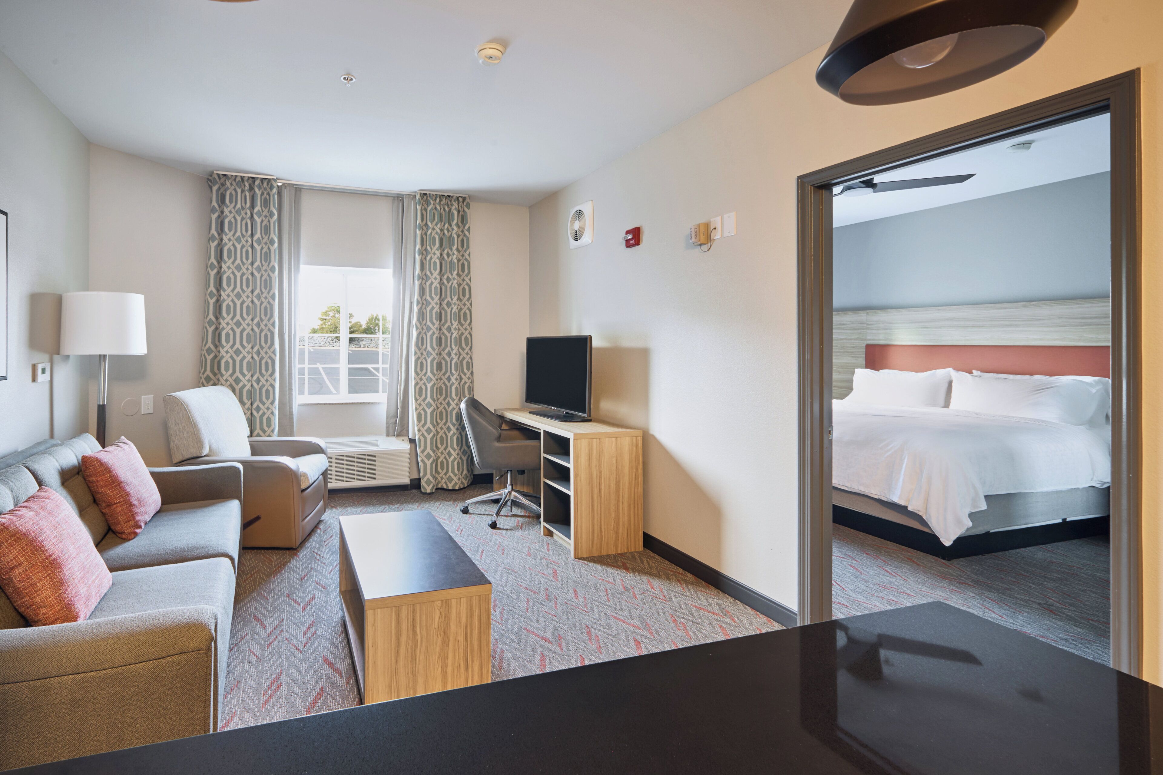 A hotel room with a bed, a desk, a chair, a television, and a view of the sea through an open door.