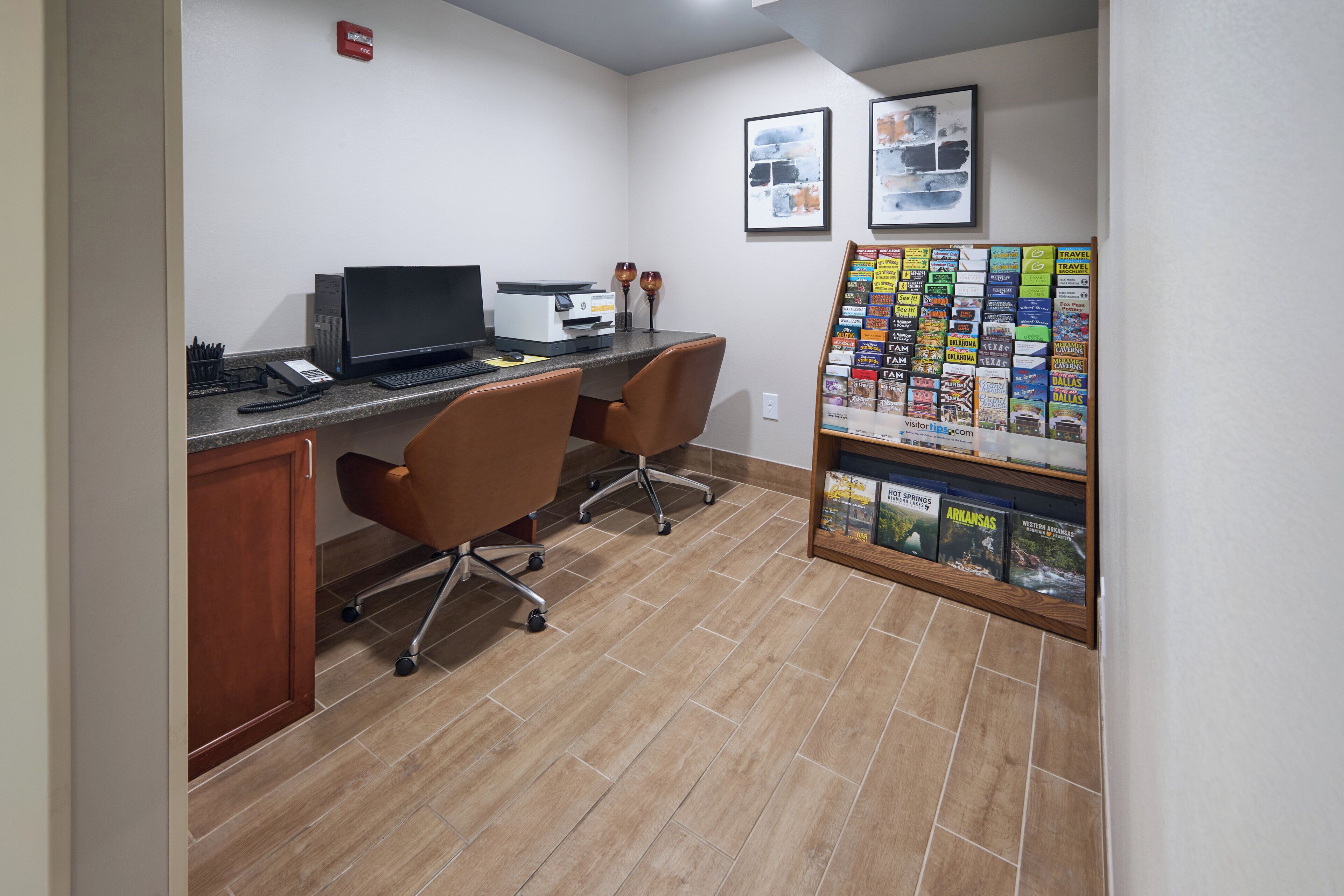 Un petit bureau avec un bureau, deux chaises, un ordinateur et un tableau d’affichage où sont accrochées des brochures de voyage.