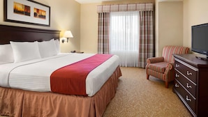 A hotel room with a large bed, a television, a chair, a dresser, and a window with curtains.