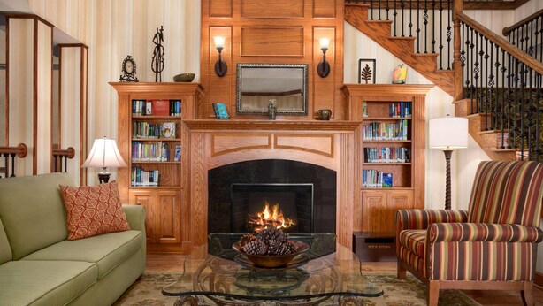 A living room with a fireplace, bookshelves, a sofa, a chair, and a staircase.