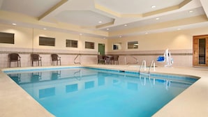 An indoor swimming pool with clear water, surrounded by chairs and a table.