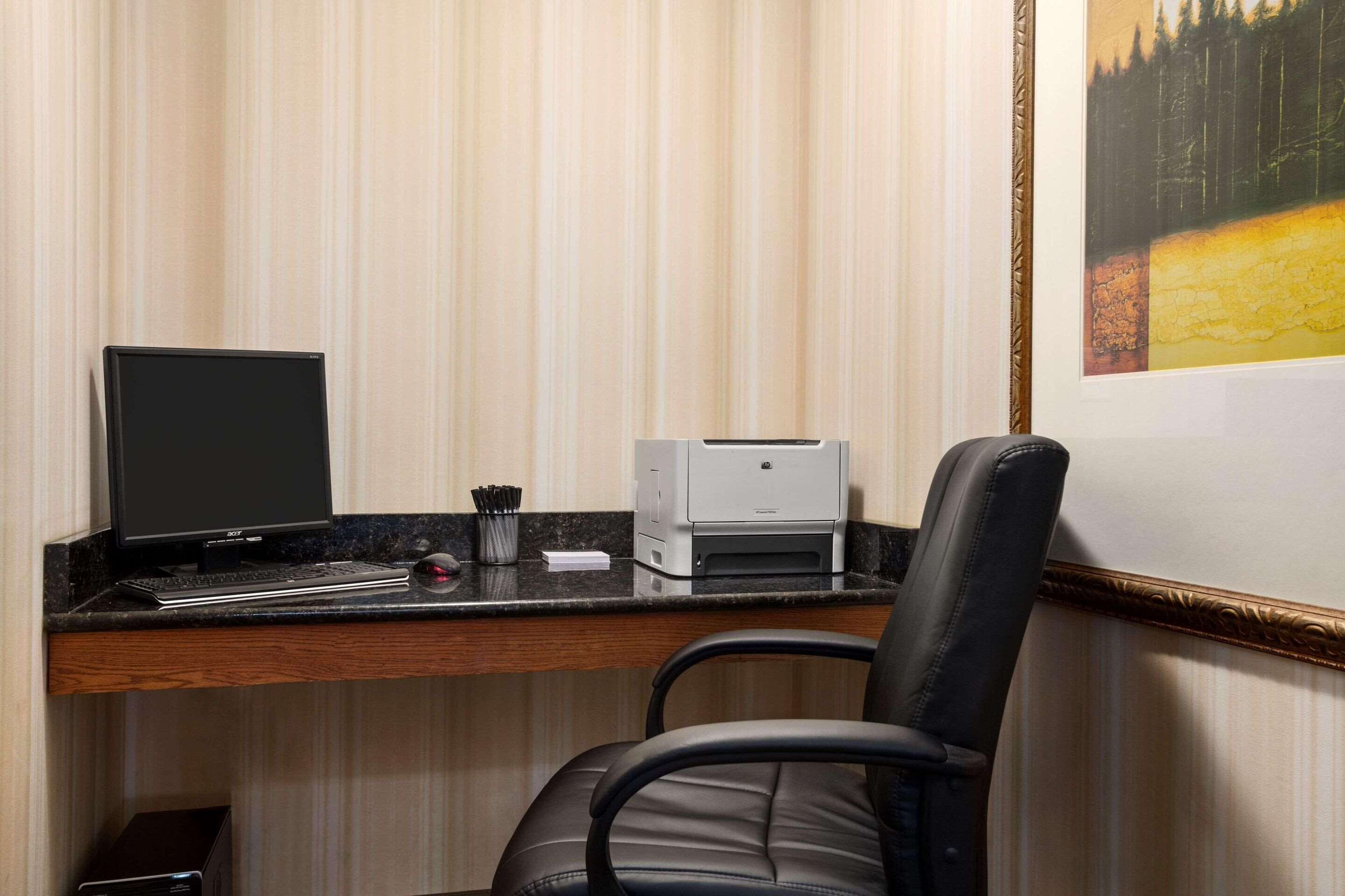A hotel office with a desk, computer, printer, and a chair.