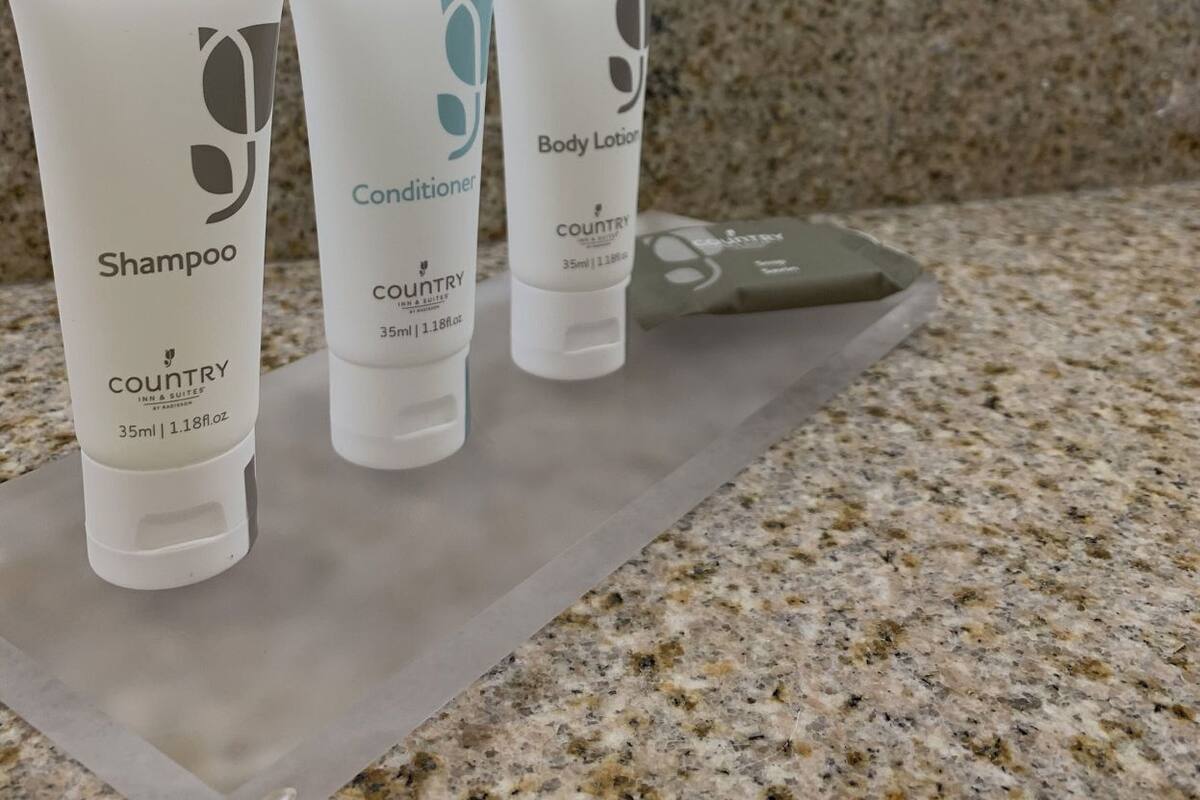 Tres botellas de artículos de aseo sobre una encimera con baldosas decorativas al fondo.
