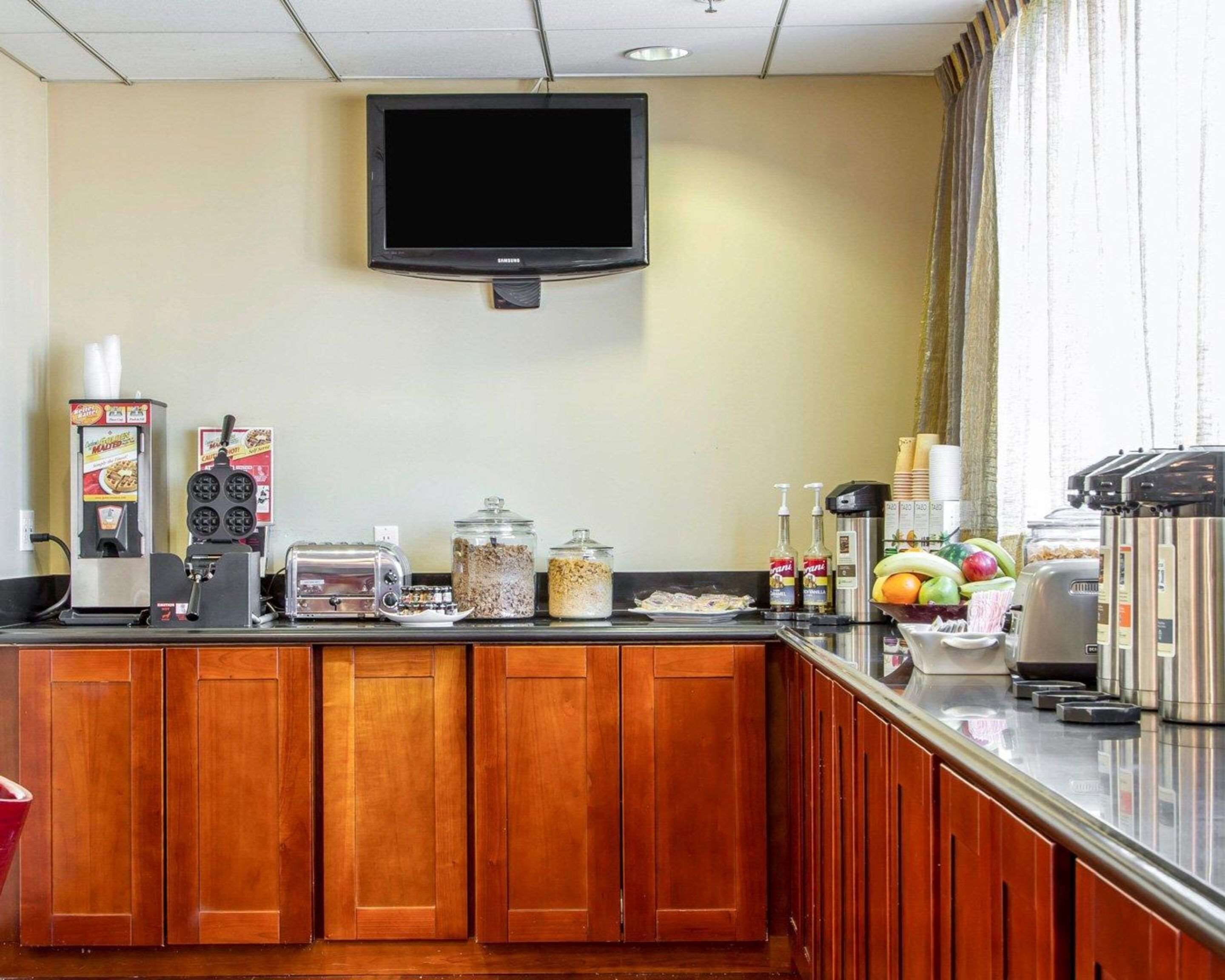 Una barra de desayuno con un televisor de pantalla plana encima, diferentes dispensadores de comida y bebida, y un frutero.
